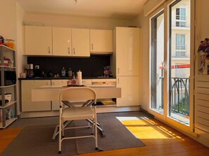 Eine moderne Küche mit weißen Schränken, einem Essbereich mit einem Stuhl und einem großen Fenster mit Blick nach draußen.