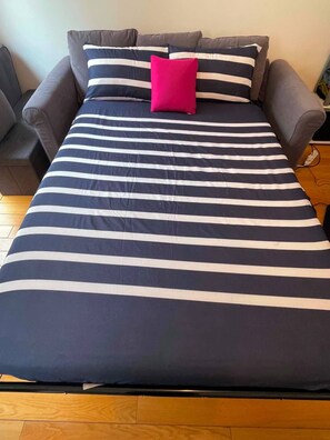 Ein Bett mit einer gestreiften Bettdecke und einem einzelnen, leuchtend pinkfarbenen Kopfkissen.