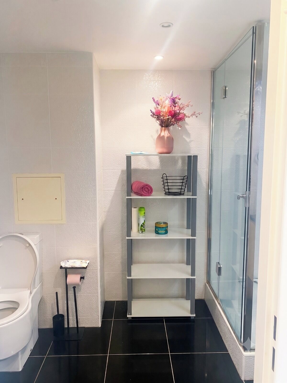 Et badeværelse med toilet, brusebad og en hylde med toiletartikler.