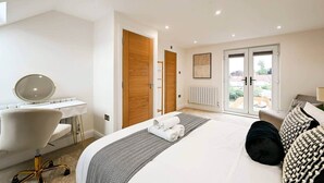 A modern bedroom with a bed, bedside table, chair, and a view of the outside through a glass door. - 5BR Family Home | Garden | AC | Near Wembley (Greenford)