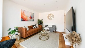 A modern living room with a brown sofa, a round coffee table, and a large abstract painting on the wall. - 5BR Family Home | Garden | AC | Near Wembley (Greenford)