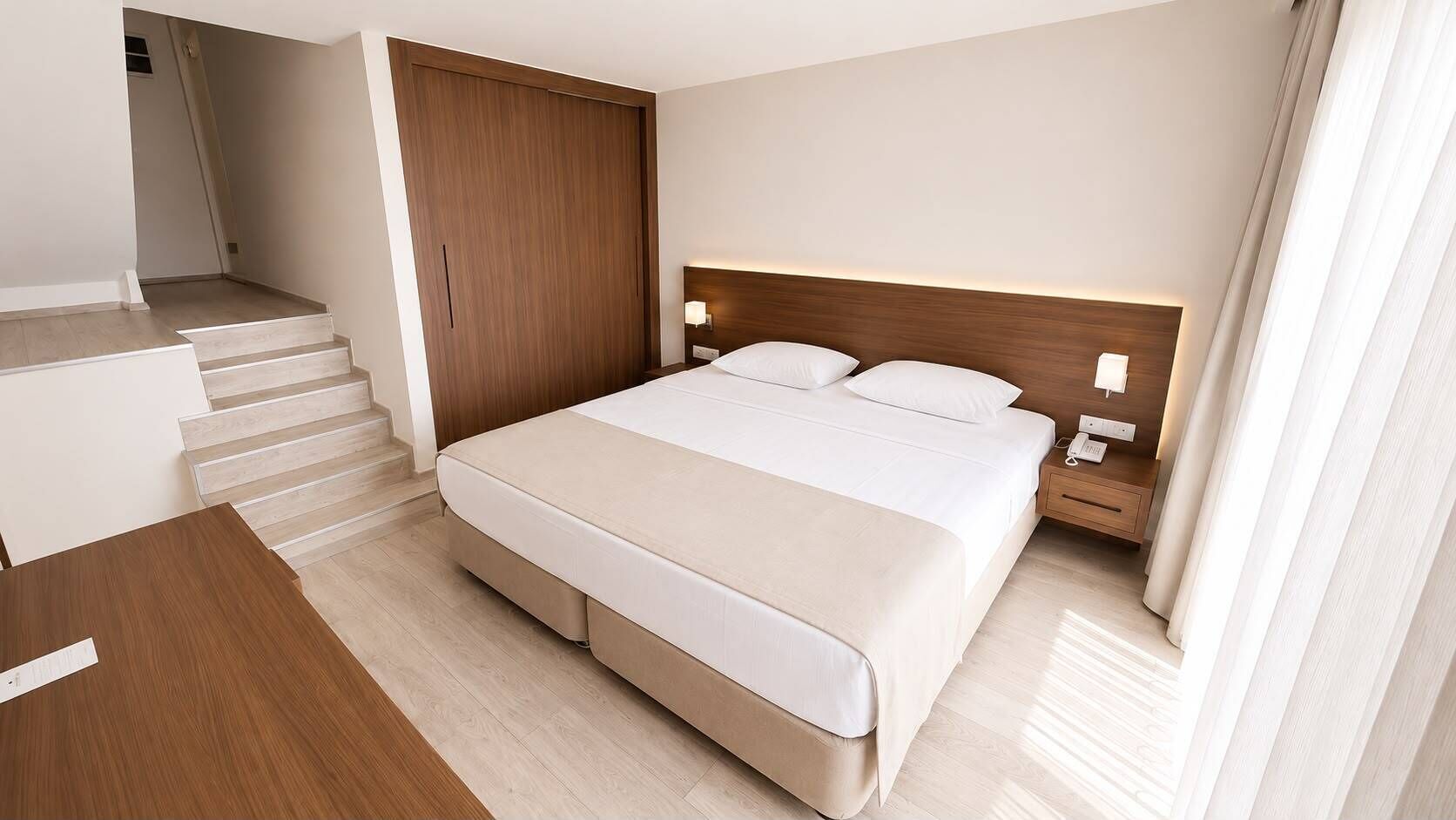 A hotel room with a bed, bedside table, nightstand, and a staircase leading to an upper floor.