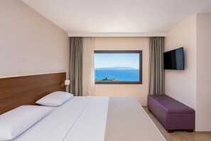 Quarto de hotel com cama, televisão na parede e janela com vista para o mar.