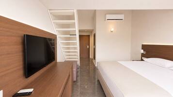 Una habitación de hotel con cama, televisión sobre un escritorio de madera, una escalera y un equipo de aire acondicionado.