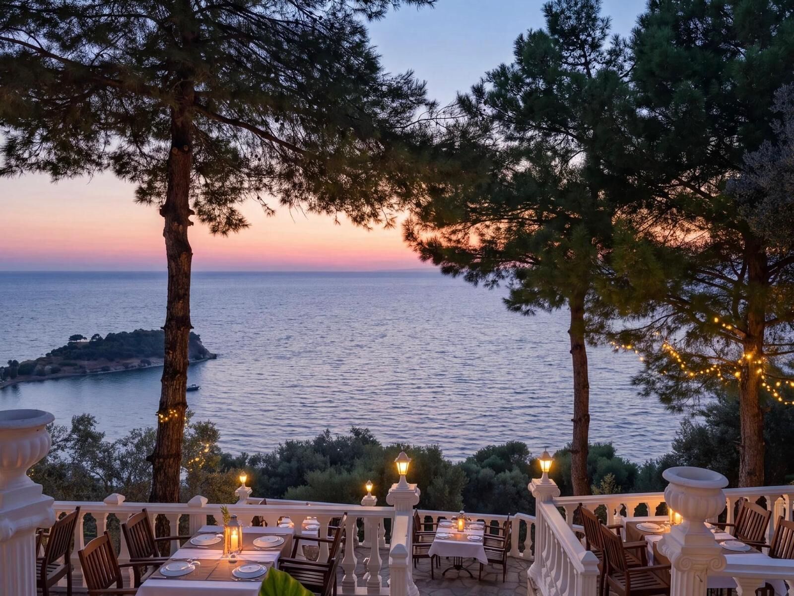 An outdoor dining area with tables set for two, overlooking a body of water and a distant island.