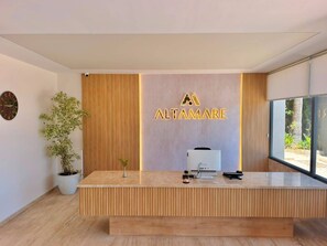 A reception desk with a wooden finish, a potted plant, and a wall-mounted sign for Altamare. - ALTAMARE HOTEL (Kusadasi)