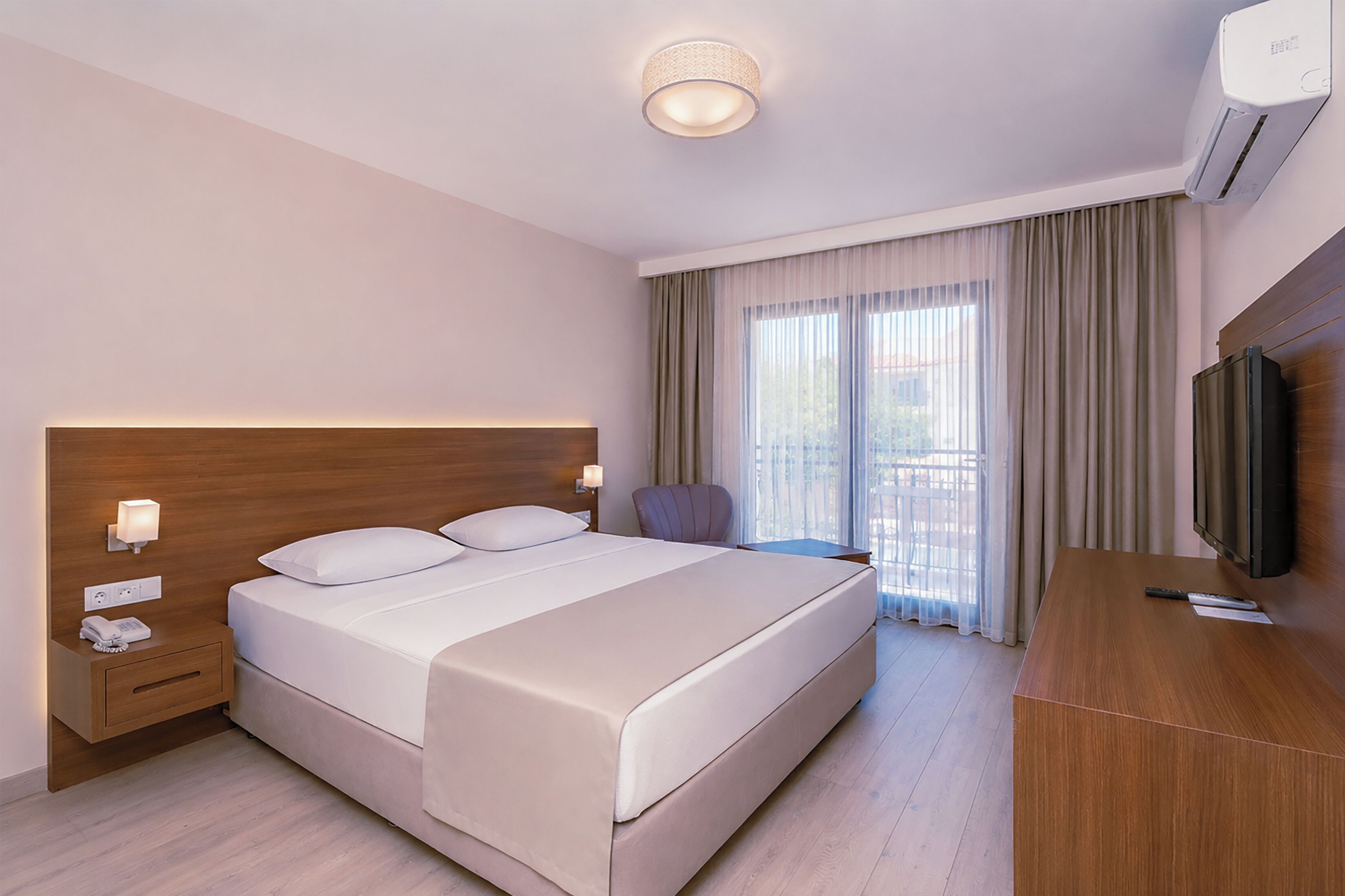 A hotel room with a large bed, bedside lamps, a desk, a chair, a TV, and a balcony with curtains.