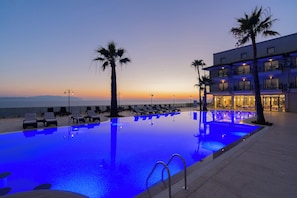 Una piscina amb gandules, palmeres i un edifici amb balcons.