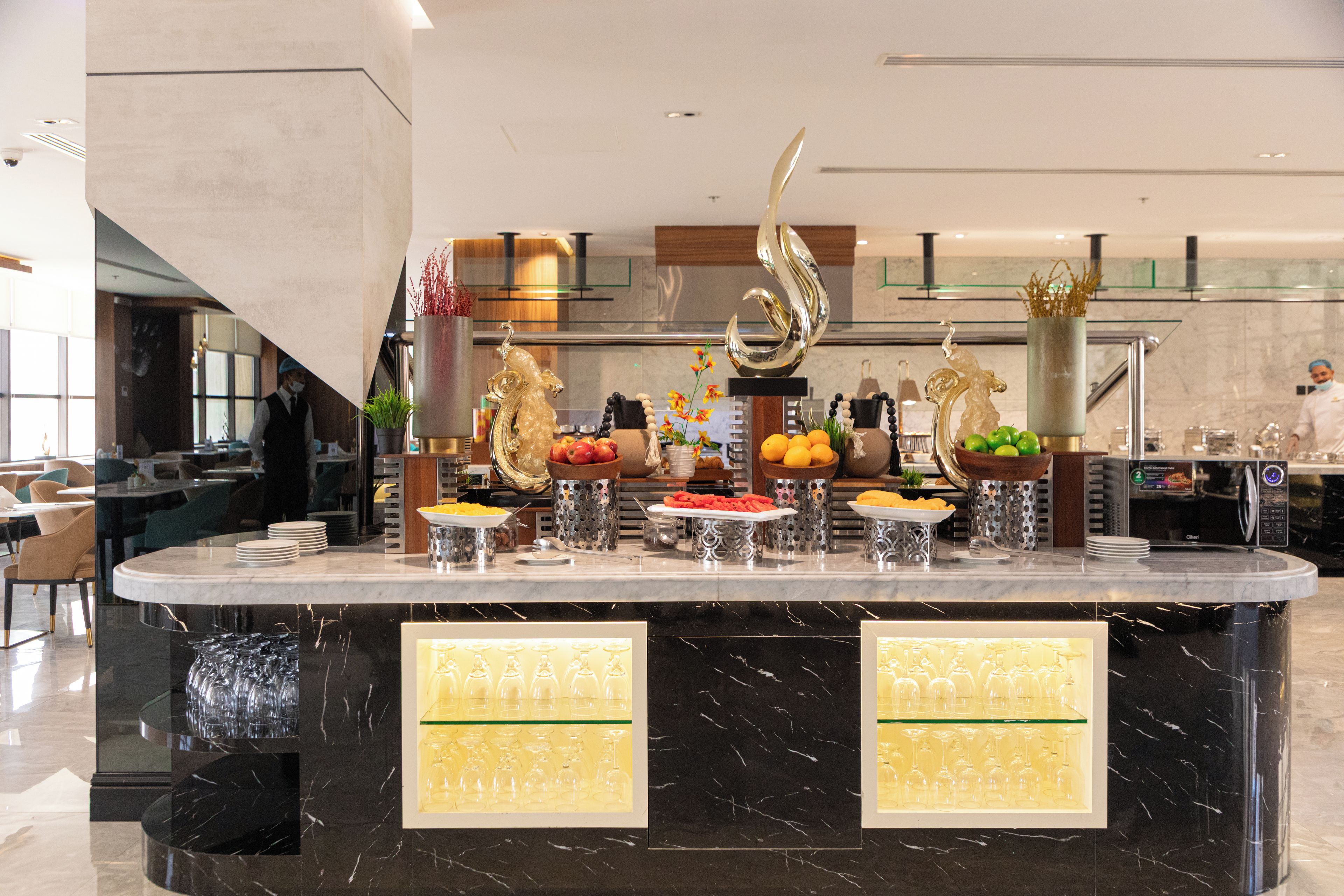 Een buffetopstelling met diverse gerechten en bestek, een decoratief metalen beeldhouwwerk en een moderne keuken op de achtergrond.