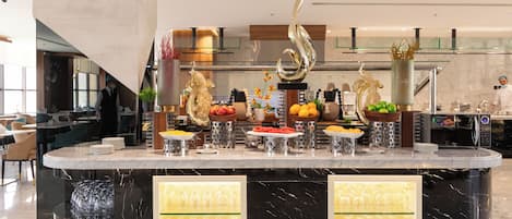 Ein reichhaltiges Buffet mit verschiedenen Speisen und Besteck, eine dekorative Metallskulptur und ein moderner Küchenbereich im Hintergrund.