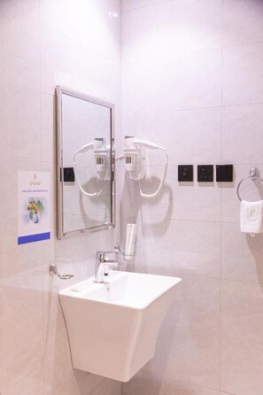A bathroom with a white sink, a mirror, and two hair dryers mounted on the wall. - Holliday Alkhaleej (Riyadh)