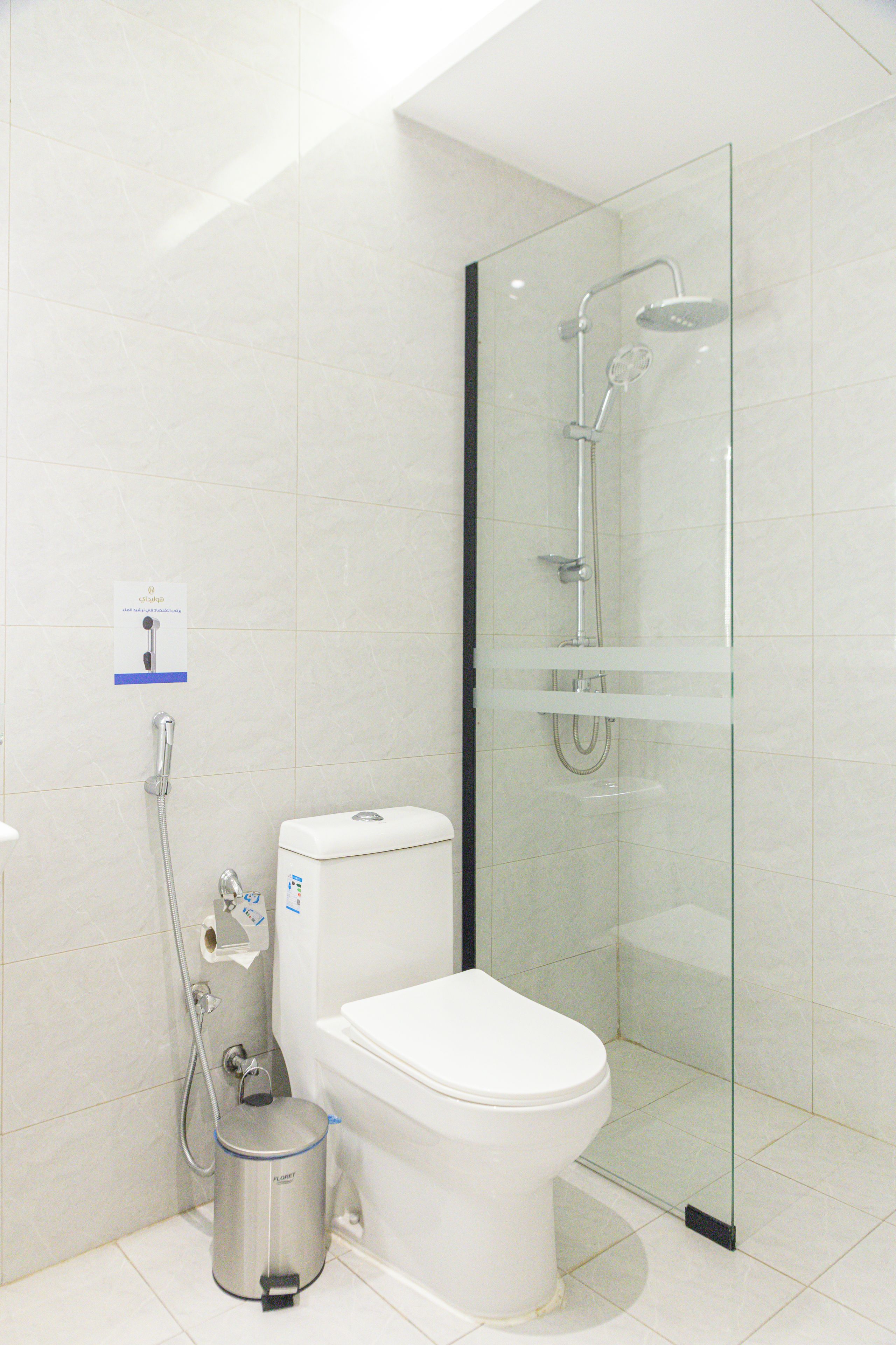 Een moderne badkamer met toilet, een douche met glazen wand en een afvalbak.