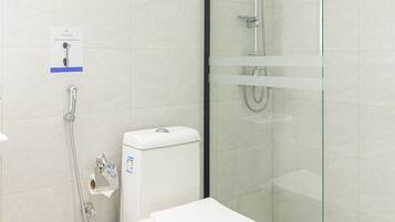 A modern bathroom with a toilet, a glass-enclosed shower, and a trash can.