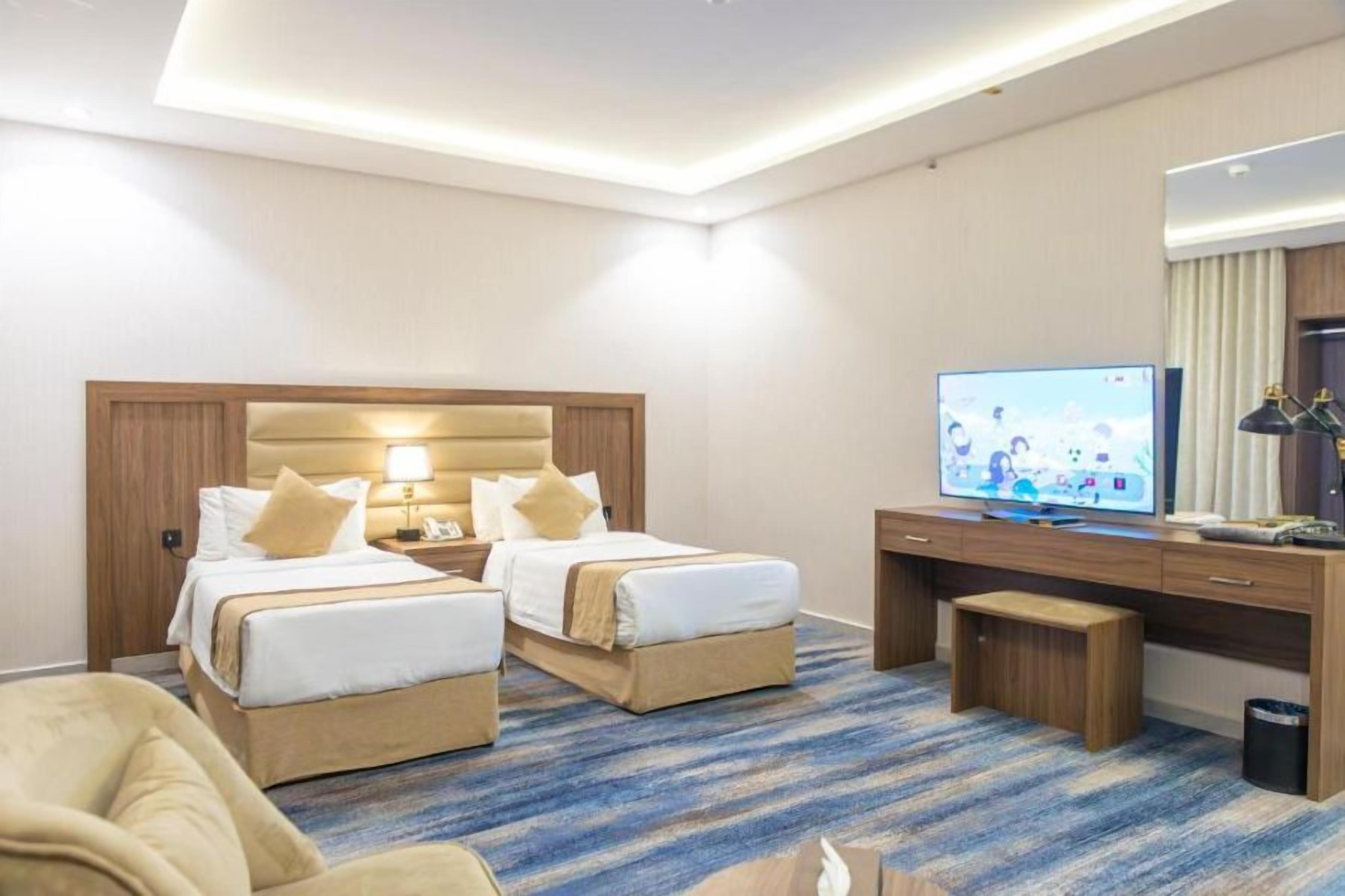 A hotel room with two beds, a desk, a television, and a carpeted floor.