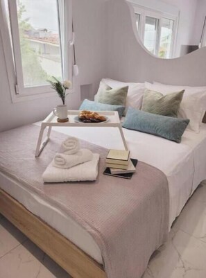 A neatly made bed with a tray of towels and a book, a window with a view, and a bedside table with a vase. - Junior Suite with heated Infinity Pool (Sozopoli)