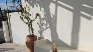 Une terrasse avec deux poufs en osier, un banc blanc et une plante en pot.