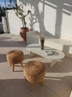 A patio area with a white sofa, two wicker ottomans, a small table with a magazine, and a potted plant. - Junior Suite with heated Infinity Pool (Sozopoli)