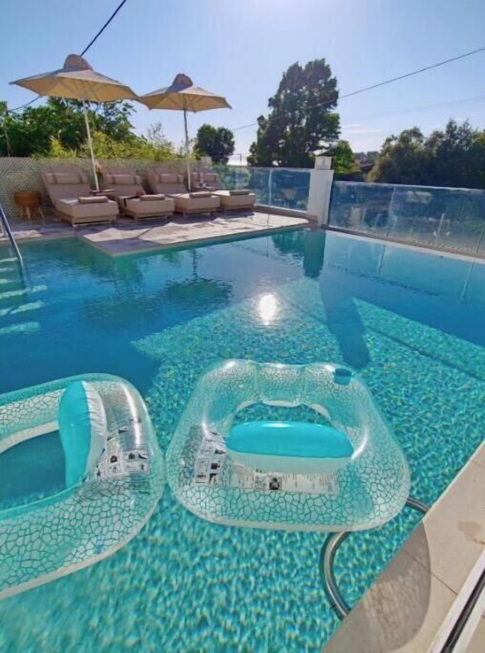Piscina con sillas de descanso y sombrillas, un jacuzzi y un cielo azul despejado.