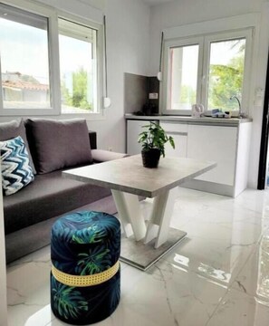 A modern kitchen with a dining area, a sofa, and a small round ottoman. - Junior Suite with heated Infinity Pool (Sozopoli)