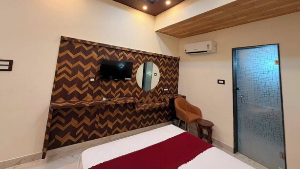 Habitación de hotel con cama, televisor montado en una pared con diseño en forma de V, una mesita, una silla y una puerta con motivo geométrico.