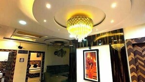 Vestíbulo de hotel con piso de mármol, una araña y un mostrador de recepción, además de un cuadro en la pared.