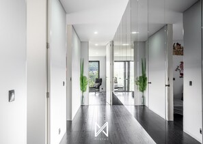 A modern hallway with a wooden floor, white walls, and glass doors leading to a balcony with a view. - MyStay - Varanda de Basto (Canedo de Basto)