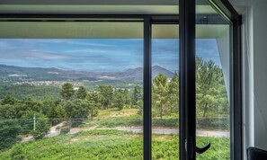 Una habitació amb un gran finestral que ofereix vistes a un paisatge verd amb arbres i un camí.