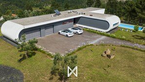 A modern building with a curved roof, two cars parked in front, a swimming pool, and a view of a mountainous landscape. - MyStay - Varanda de Basto (Canedo de Basto)
