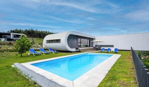 Una casa moderna amb piscina, gandules blaves i un jardí.
