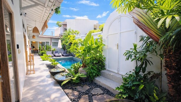 A pool area with a stone pathway, surrounded by lush greenery and a white building. - Luxury 3-BR Villa, Canggu Berawa , Private Pool (Kec. Kuta Utara)