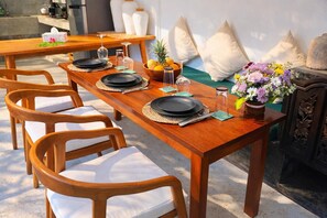 Une table de salle à manger en bois, mise avec des assiettes, des verres et un saladier rempli de fruits.