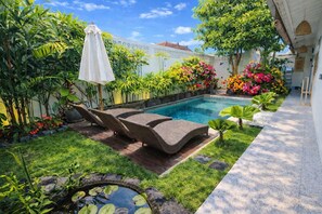Ein Schwimmbecken mit Liegestühlen und Sonnenschirm, umgeben von üppiger Vegetation und blühenden Pflanzen.