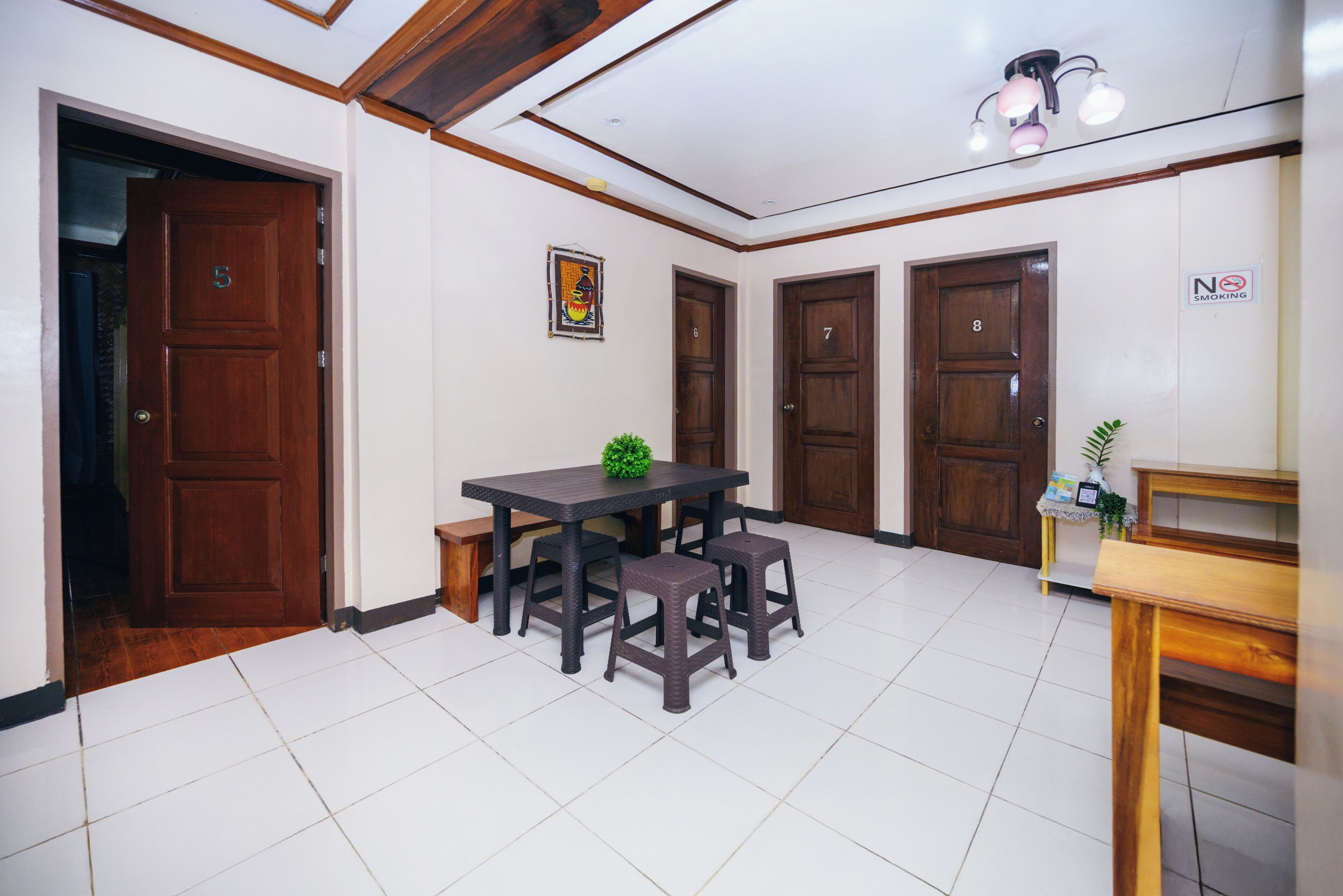A room with a dining table, four chairs, a small plant, and a 'No Smoking' sign on the wall.