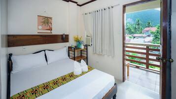 A hotel room with a bed, a small table, a vase with flowers, a window with curtains, and a view of the outside.