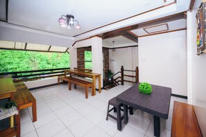 A dining area with a wooden table and benches, a small green plant on the table, and a view of greenery outside. - Silverise Guest House (El Nido)