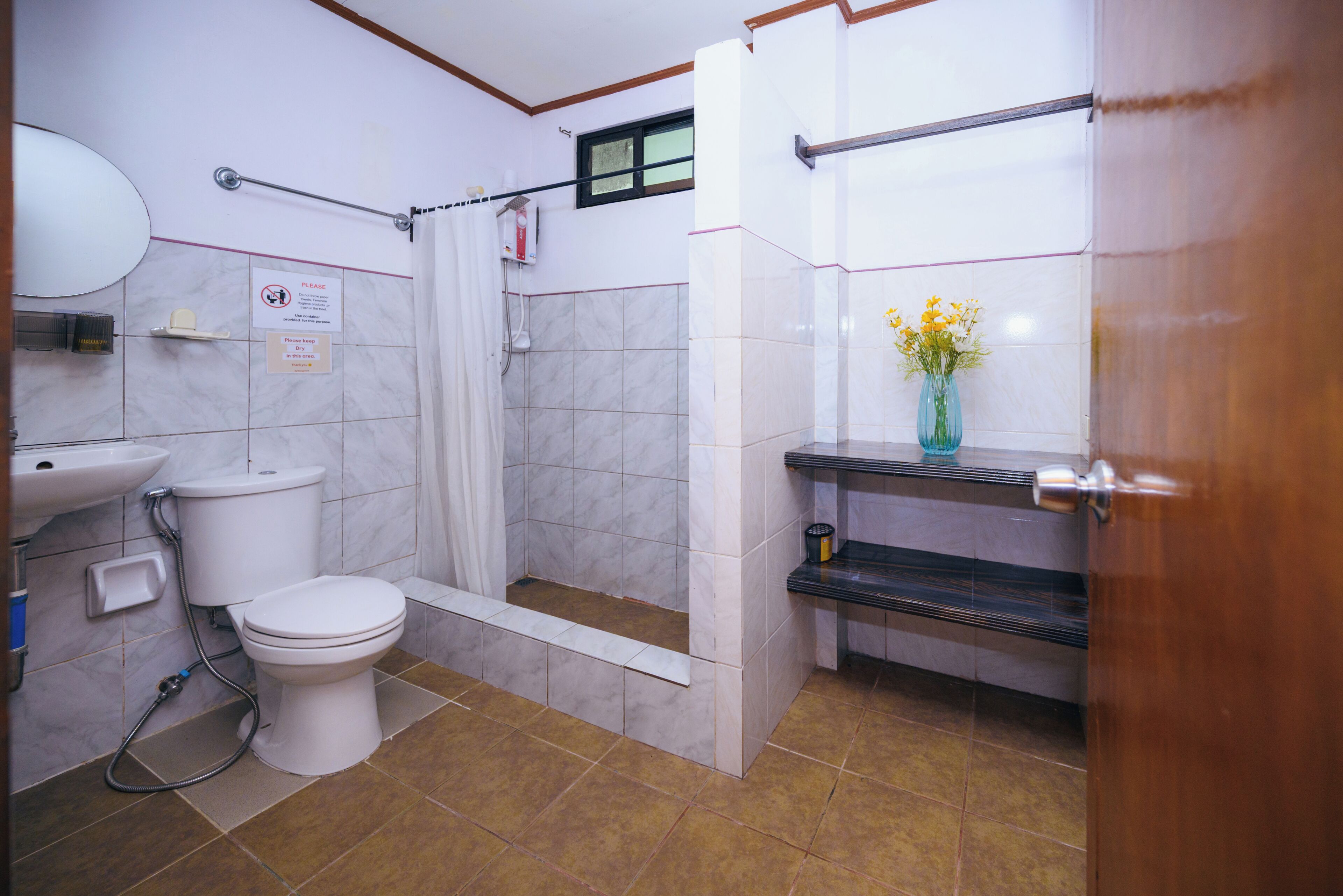 A bathroom with a toilet, shower, sink, and a vase with flowers on the counter.