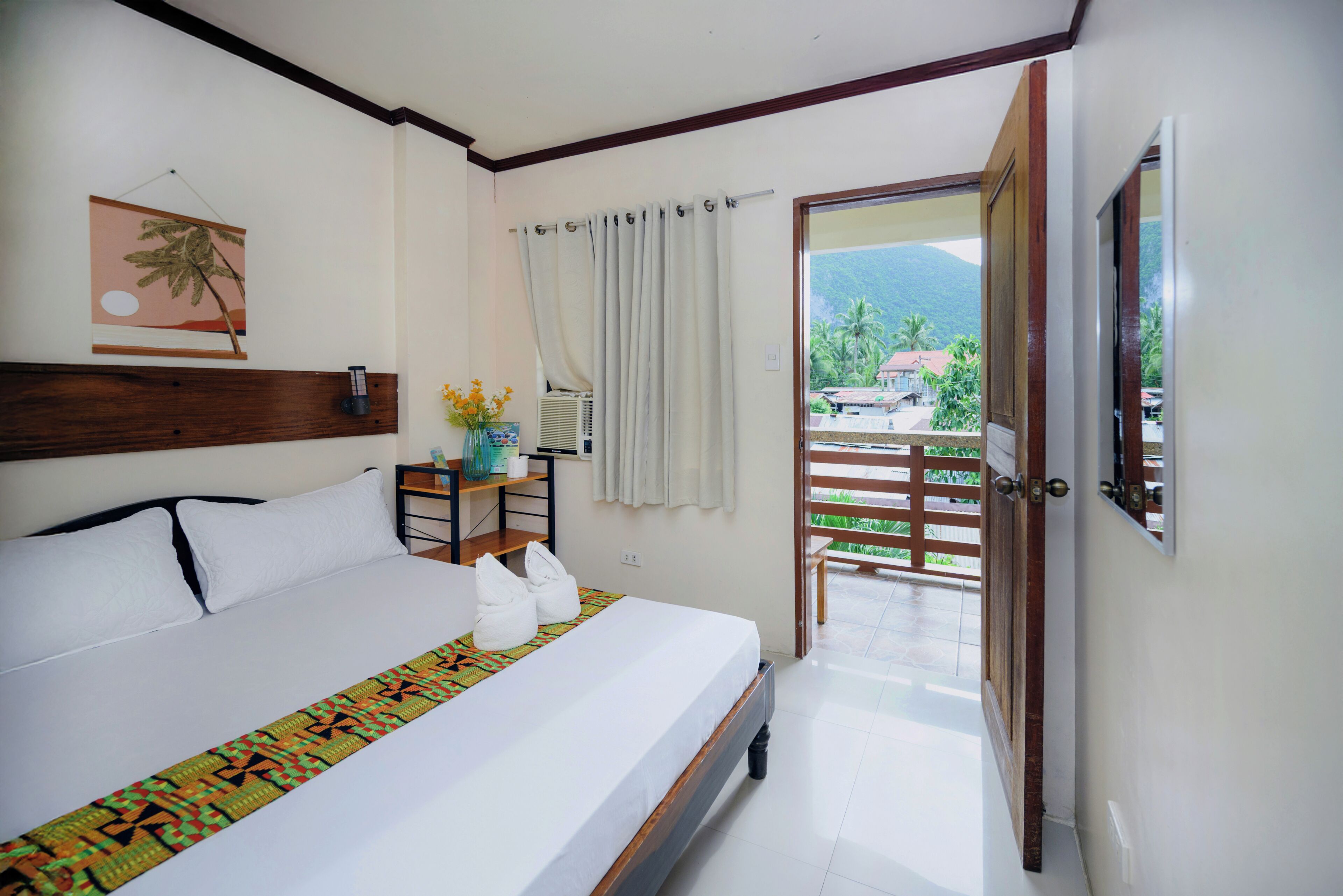 A hotel room with a bed, a nightstand, a window with curtains, a view of the outdoors, and a door leading to a balcony.