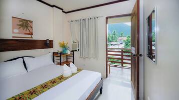 A hotel room with a bed, a nightstand, a window with curtains, a view of the outdoors, and a door leading to a balcony.