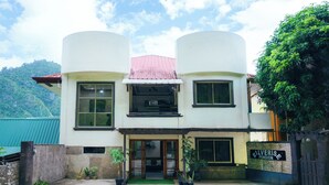 Un edificio de dos pisos con techo plano, ventanas amplias y un letrero que indica que es una pensión.