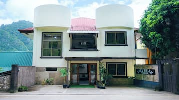 Un edificio de dos pisos con techo plano, ventanas amplias y un letrero que indica que es una pensión.