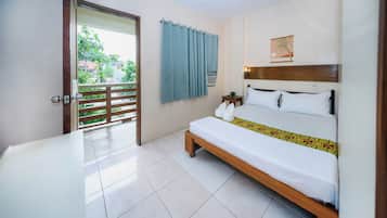 A hotel room with a bed, a small table, a wall-mounted air conditioner, and a view of greenery outside.