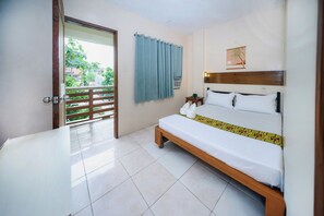 A hotel room with a bed, a small table, a wall-mounted air conditioner, and a view of greenery outside.