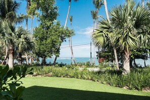 A coastal landscape with palm trees, a grassy area, and a view of the ocean. - Beachfront 2BR Condo w/ Balcony • Sol de Arena E4 (Las Terrenas)