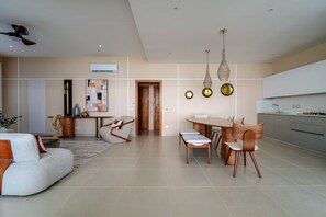 A modern living room with a sofa, dining table, and chairs, a kitchen with cabinets, and a ceiling fan. - Beachfront 2BR Condo w/ Balcony • Sol de Arena E4 (Las Terrenas)