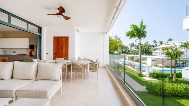 A modern living room with a balcony overlooking a pool and greenery. - Beachfront 2BR Condo w/ Balcony • Sol de Arena E4 (Las Terrenas)