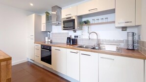 A modern kitchen with white cabinets, stainless steel appliances, and a wooden countertop. - Deluxe Two Bed Fully Serviced Apartment in ExCeL (London)