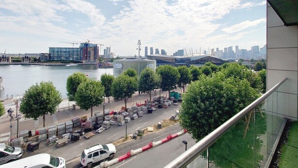 A view of a riverside area with a city skyline, trees, and parked vehicles. - Deluxe Two Bed Fully Serviced Apartment in ExCeL (London)