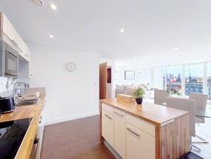 A modern kitchen with a wooden countertop, built-in appliances, and a dining area with a glass table and chairs. - Deluxe Two Bed Fully Serviced Apartment in ExCeL (London)