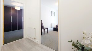 A hallway leading to a bedroom with a radiator, a chair, and a bed. - Deluxe Two Bed Fully Serviced Apartment in ExCeL (London)