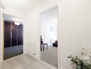 Ein Flur, der in ein Schlafzimmer führt, mit Heizkörper, Stuhl und Bett.